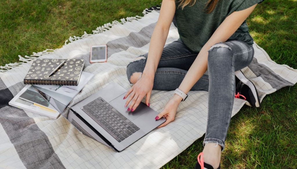 Une personne suit un cours en ligne sur un ordinateur portable, un cahier ouvert à côté du clavier.