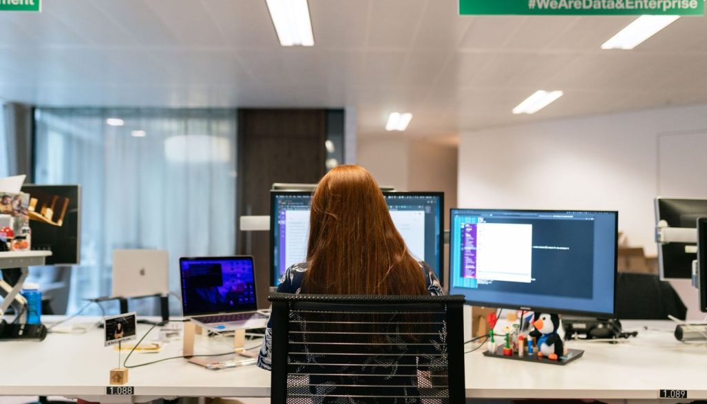 Ingénieur informaticien assis devant deux écrans de code dans un open space
